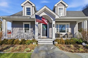 Une maison à deux étages avec un porche à l’avant, un drapeau et des meubles d’extérieur.
