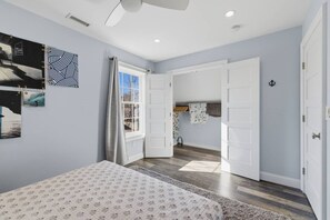 Un dormitorio con cama, ventana con cortinas, puerta y pared con cuadros.