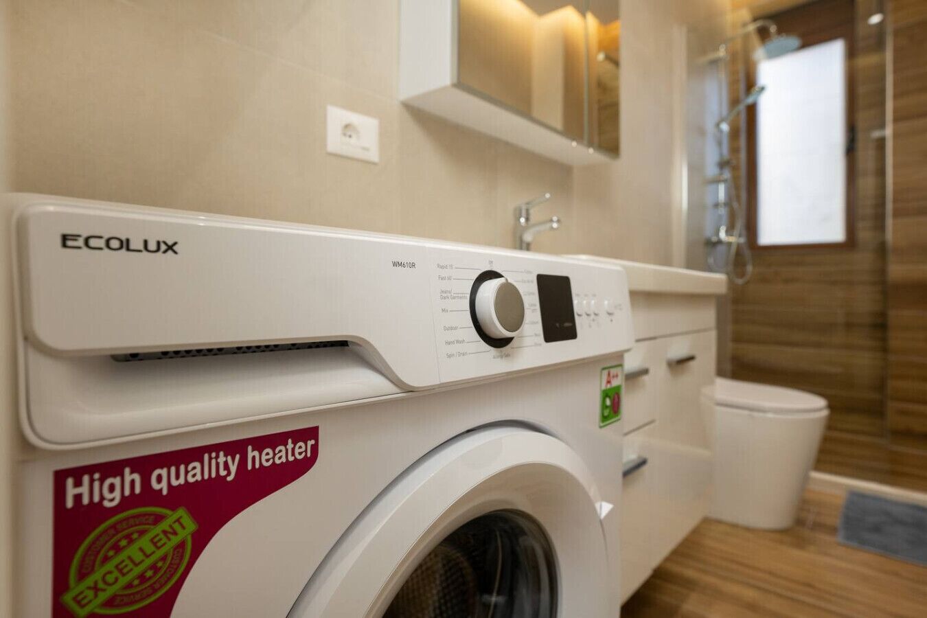 Un espace buanderie compact et moderne, équipé d’un lave-linge à chargement frontal portant la marque « Ecolux » et d’un autocollant indiquant « Chauffage de haute qualité ».