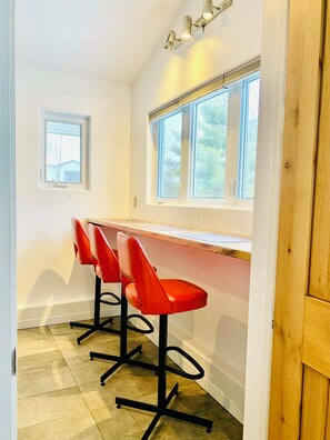 A kitchen with a wooden countertop, three red bar stools, and a window above the counter.