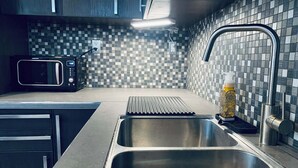 Une cuisine moderne dotée d’un évier en acier inoxydable, d’un four à micro-ondes et d’un dosseret carrelé.