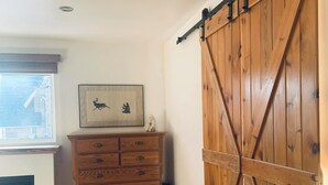 Une pièce avec une commode en bois, une grande porte coulissante de style grange, une cheminée et un tableau encadré au mur.
