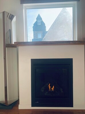 A modern living room with a fireplace, a large window, and a view of a building outside.