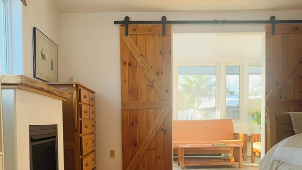 Une chambre dotée d’une grande porte coulissante de style grange, d’une cheminée, d’un lit et offrant une vue sur l’extérieur.