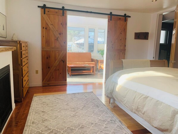 A bedroom with a bed, a wooden dresser, a sliding barn door, and a view of the outside.