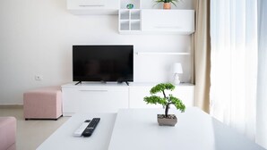 Una sala de estar moderna con una televisión de pantalla plana, una planta pequeña en maceta, un control remoto y un otoman rosa.