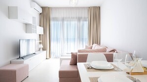 Una sala de estar moderna con un sofá, una mesa de comedor dispuesta con platos y vasos, y un televisor sobre un mueble.