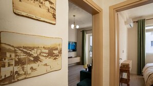 Ein Hotelzimmer mit Bett, Sessel, Schreibtisch und Fernseher. An der Wand hängen zwei Vintage-Fotos.
