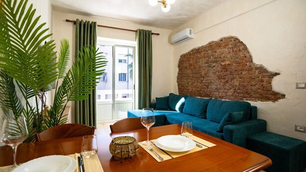 Ein Essbereich mit einem Holztisch, gedeckt für zwei Personen, einem blauen Sofa und einer Ziegelwand.