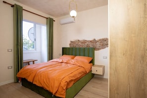 Ein Schlafzimmer mit einem grünen Bett, orangefarbener Bettwäsche, einer Ziegelwand und einem Fenster mit Vorhängen.