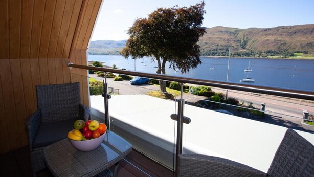 A balcony with a view of a lake, a tree, and a table with a bowl of fruit. - Loch View Apartment in Fort William Town Centre (Fort William)