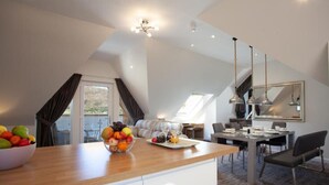 A modern kitchen with a fruit bowl, dining area with a table and chairs, and a large mirror. - Loch View Apartment in Fort William Town Centre (Fort William)