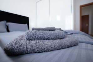 Un lit bien fait, avec une couverture et des oreillers gris, une tête de lit noire et une fenêtre avec des rideaux.