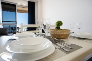 Une table à manger dressée avec des assiettes, des couverts et des verres, agrémentée d’une petite plante en pot dans un panier tressé.