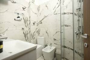 Une salle de bain avec un pare-baignoire en marbre, des toilettes, un bidet, une douche et un lavabo.