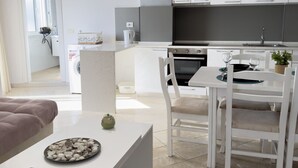 A modern kitchen with white cabinets, a dining area with a white table and chairs, and a living area with a sofa and a coffee table. - Terrace View Apartment Durres (Durrës)