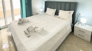 A modern hotel room with a large bed, two bedside tables, a nightstand, and a view of the outside through a sliding glass door. - Terrace View Apartment Durres (Durrës)