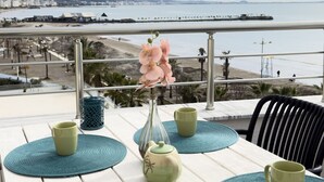 A table set with green cups and a vase with pink flowers, overlooking a beach and cityscape. - Terrace View Apartment Durres (Durrës)