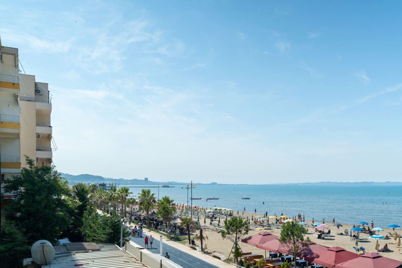 Una playa con sombrillas y gente, un cielo despejado y una vista distante del mar.