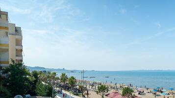 Una playa con sombrillas y gente, un cielo despejado y una vista distante del mar.