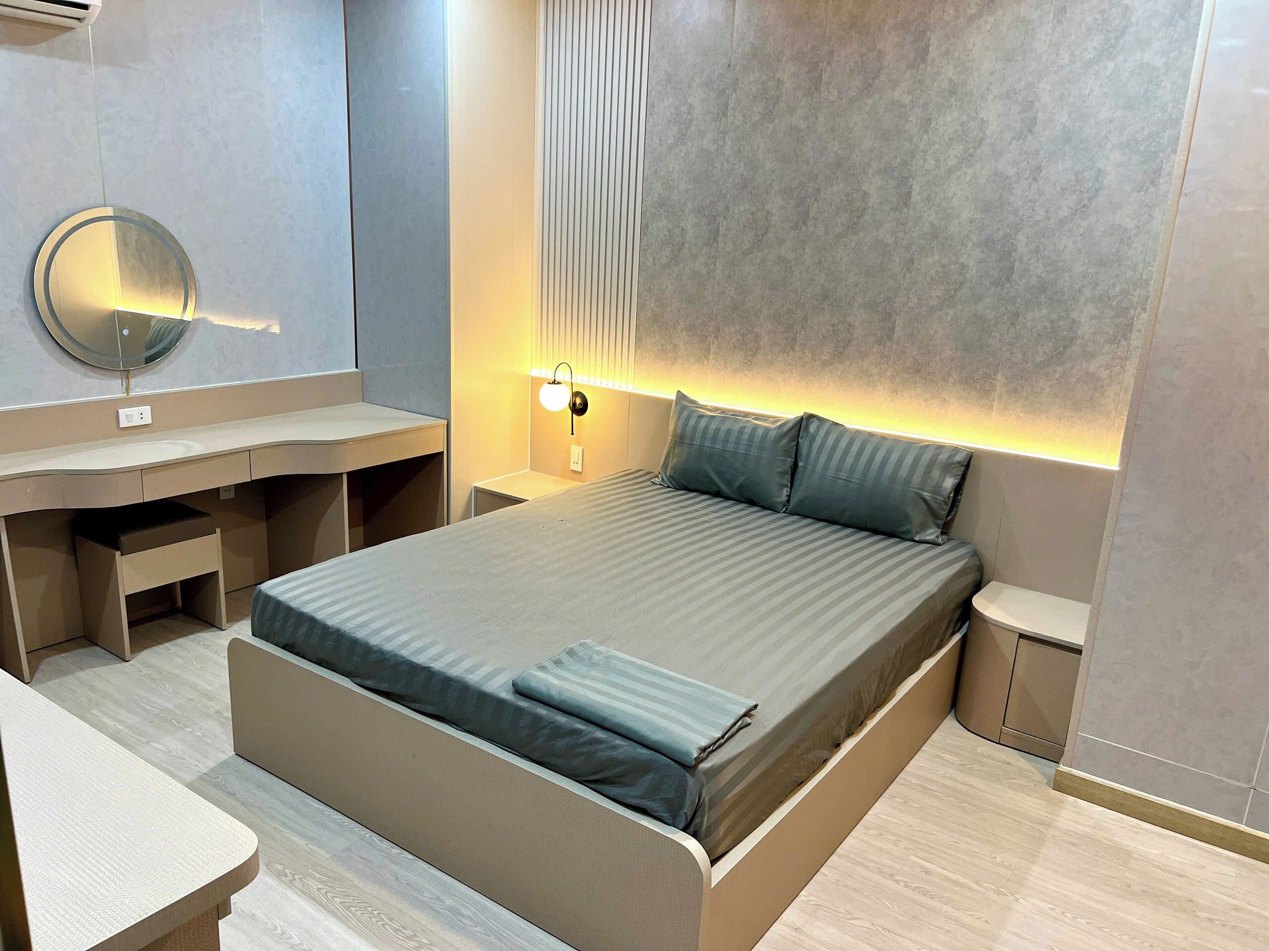 Een moderne slaapkamer met een bed, nachtkastjes, een bureau en een wandlamp.