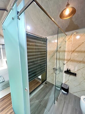 Uma casa de banho moderna com cabine de duche em vidro, paredes de mármore e soalho em madeira.