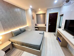 Quarto moderno com cama, mesa de cabeceira, escrivaninha e televisão.