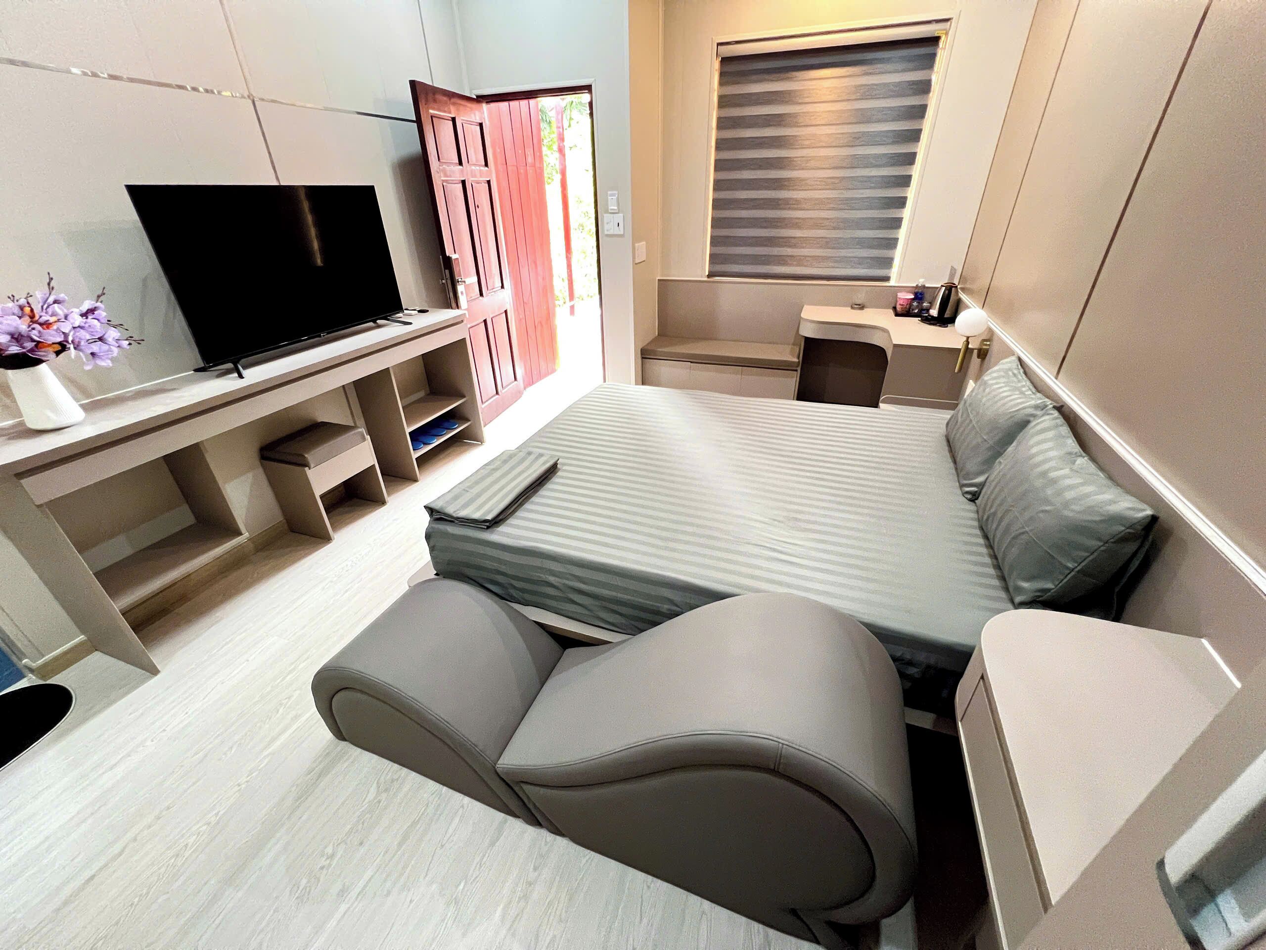 A compact room with a bed, a TV, a desk, and a small seating area.