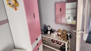Une chambre d’enfant avec des meubles roses, un miroir et des peluches.