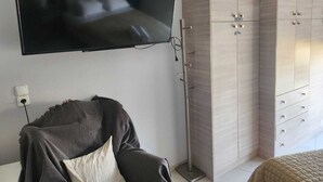 Une chambre à coucher avec un téléviseur fixé au mur, une armoire à plusieurs portes et un lit avec une couverture et un oreiller.