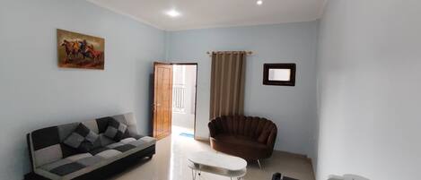 Una sala de estar con un sofá, un sillón marrón, una mesa de centro y un cuadro en la pared.