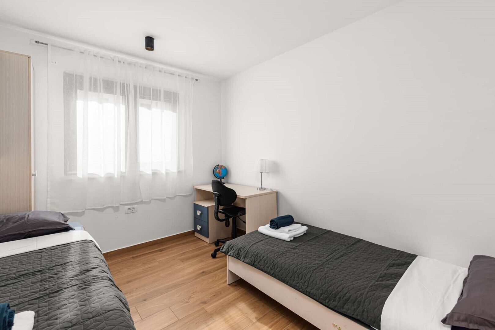 Une chambre avec deux lits, un bureau, un globe terrestre et une lampe.