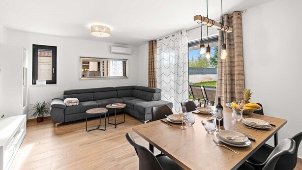 A modern living room with a grey sectional sofa, a dining table set for four, and a large window with curtains. - Apartment EM – Peaceful Stay near Poreč for 4 Guests (Poreč)