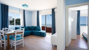 Un salon moderne avec un canapé d’angle bleu, une table à manger avec des chaises et de grandes fenêtres donnant sur la mer.