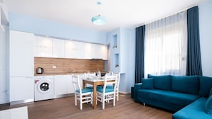 Un appartement moderne comprenant un coin repas, un salon avec un canapé bleu, une cuisine avec des meubles blancs et un lave-linge.