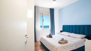 Une chambre à coucher avec un lit, une fenêtre avec des rideaux, une vue sur la mer et une porte.