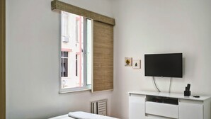 Una camera da letto con un letto, una ventola a soffitto, una TV e una finestra con persiane.