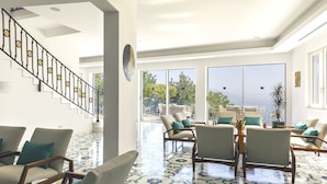Amplia sala de estar con escaleras, ventanas grandes y suelo de baldosas.