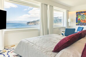 Ein Hotelzimmer mit Bett, Schreibtisch, Sessel, Fernseher und einem Fenster mit Blick auf das Meer und die Klippen.
