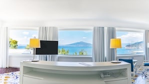 Habitación de hotel con escritorio, dos lámparas, televisión de pantalla plana, teléfono y vista al mar.