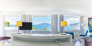 Ein Hotelzimmer mit Schreibtisch, zwei Lampen, einem Flachbildfernseher, einem Telefon und Meerblick.