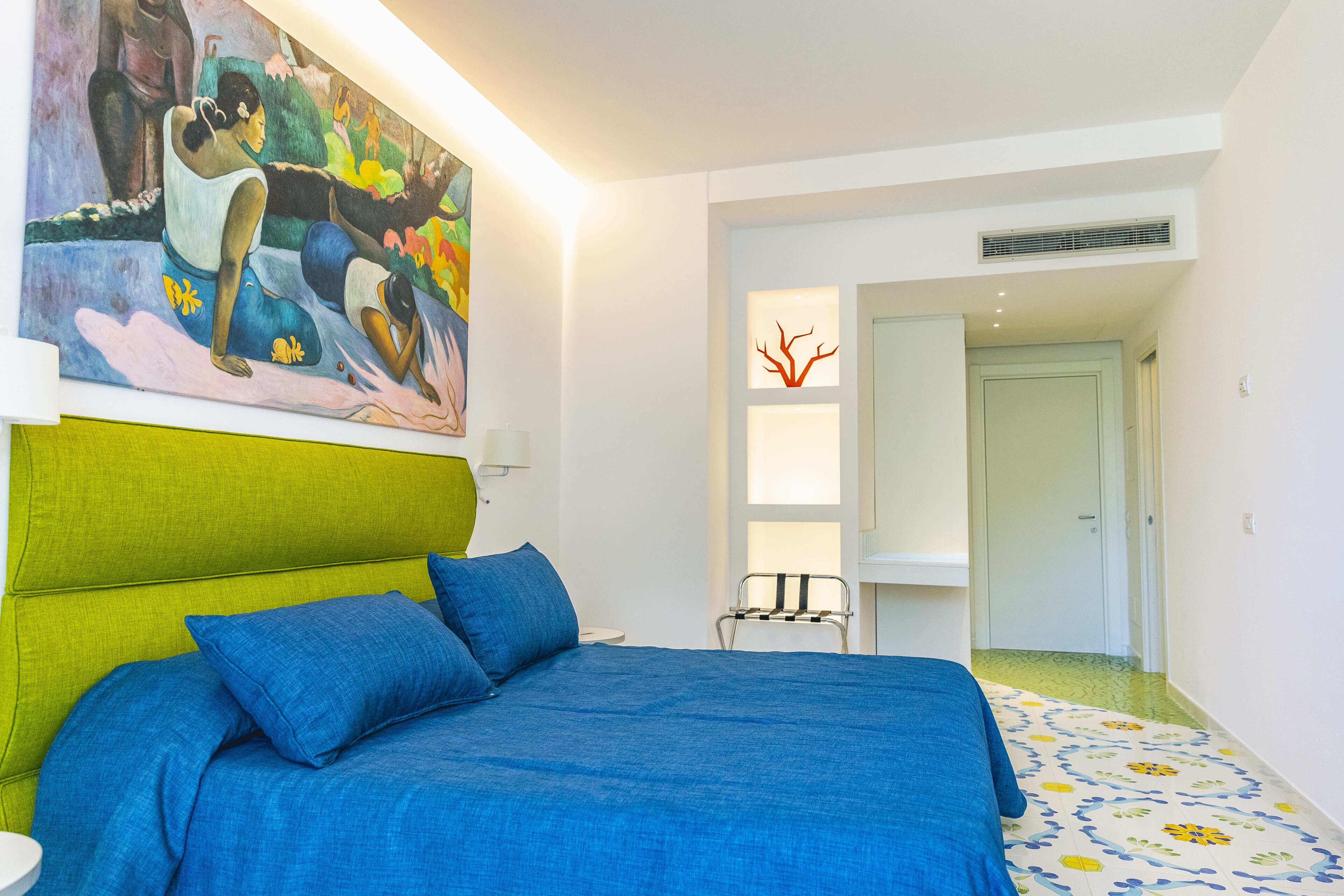 A bedroom with a bed, a green headboard, a painting, a chair, and a door leading to another room.