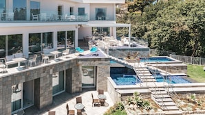 Una casa moderna de varios pisos con zonas de estar al aire libre, una piscina y un patio de piedra.