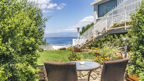 Un patio con mobiliario de mimbre, una mesa de vidrio y vista al mar.