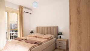 Ein Schlafzimmer mit Bett, Nachttischen, einer Lampe, einer Klimaanlage und Blick ins Freie.