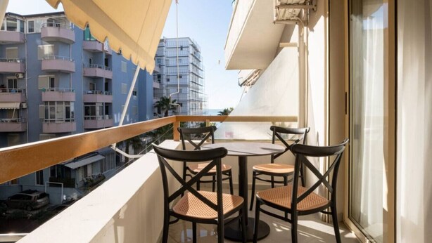 Ein Balkon mit Tisch und Stühlen, mit Blick auf eine Stadtlandschaft mit Gebäuden und blauem Himmel.