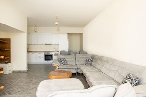 A modern living room with a sectional sofa, a wooden coffee table, and a kitchen in the background. - Bubble Trouble Duplex by TOK apartments (Durrës)