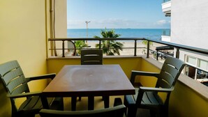 Un balcón con mesa y sillas, con vista a una playa con palmeras y el mar.