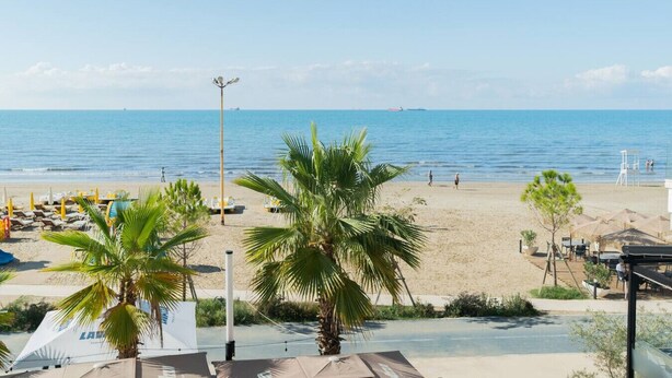 Una playa con palmeras, una torre de salvavidas y un cielo azul despejado.