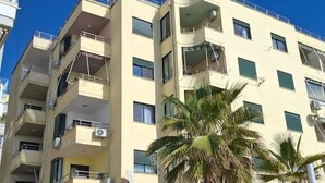 Un hotel de varios pisos con balcones, mobiliario exterior y palmeras.
